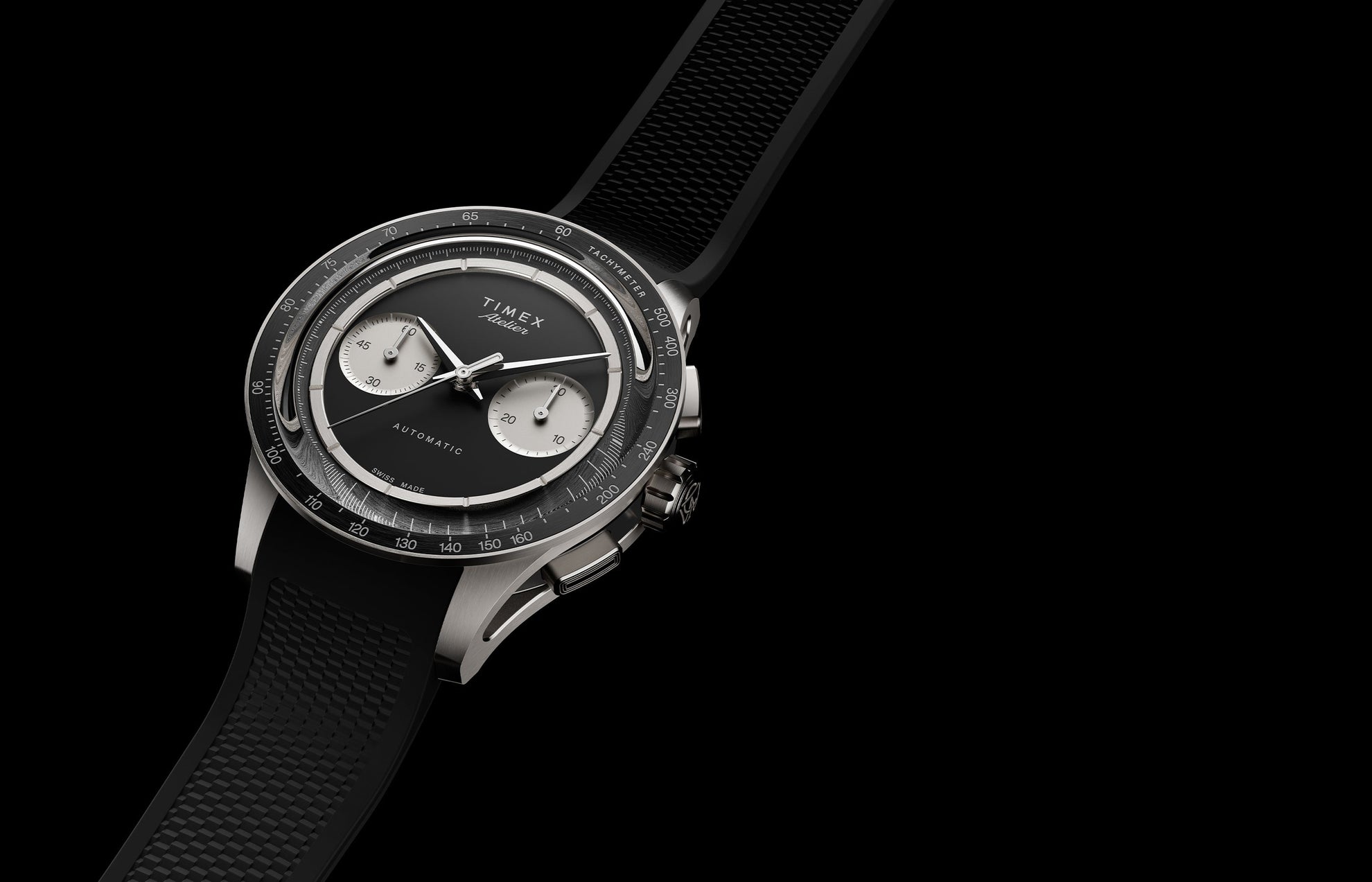 Timex Atelier Chronograph Automatic M1a Ti titanium watch with black dial, silver-tone sub-dials, tachymeter bezel, and textured black rubber strap shown at an angled perspective.
