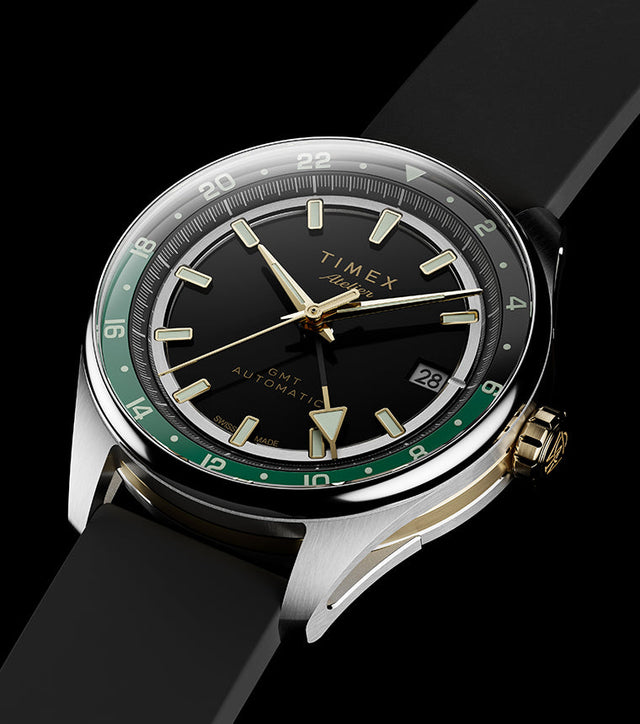 Timex Atelier GMT Première M1a watch with a black dial, green 24-hour scale, gold-tone accents, and black rubber strap.