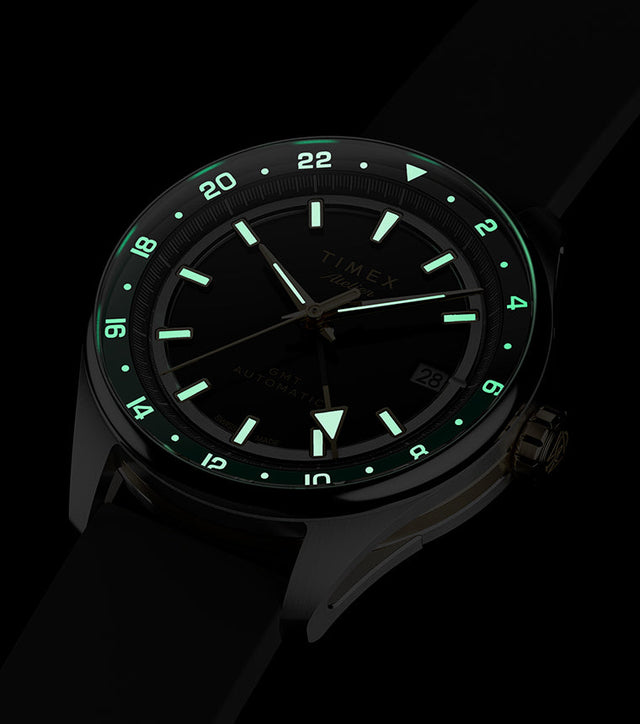 Timex Atelier GMT Première M1a watch glowing in the dark with illuminated hands, hour markers, and 24-hour scale.