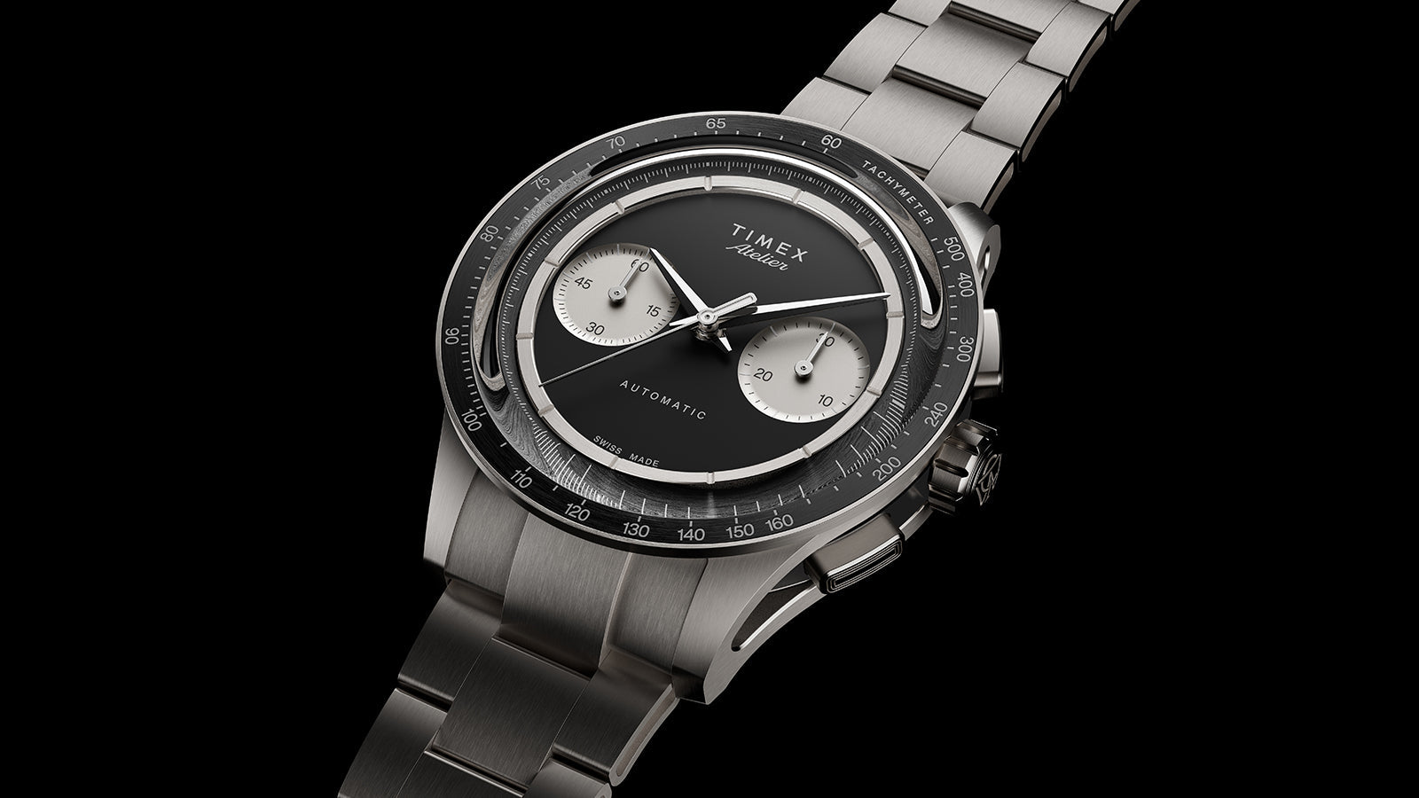 Timex Atelier Chronograph Automatic M1a Ti luxury sports watch in titanium with integrated bracelet, black dial, and tachymeter bezel against a black background.