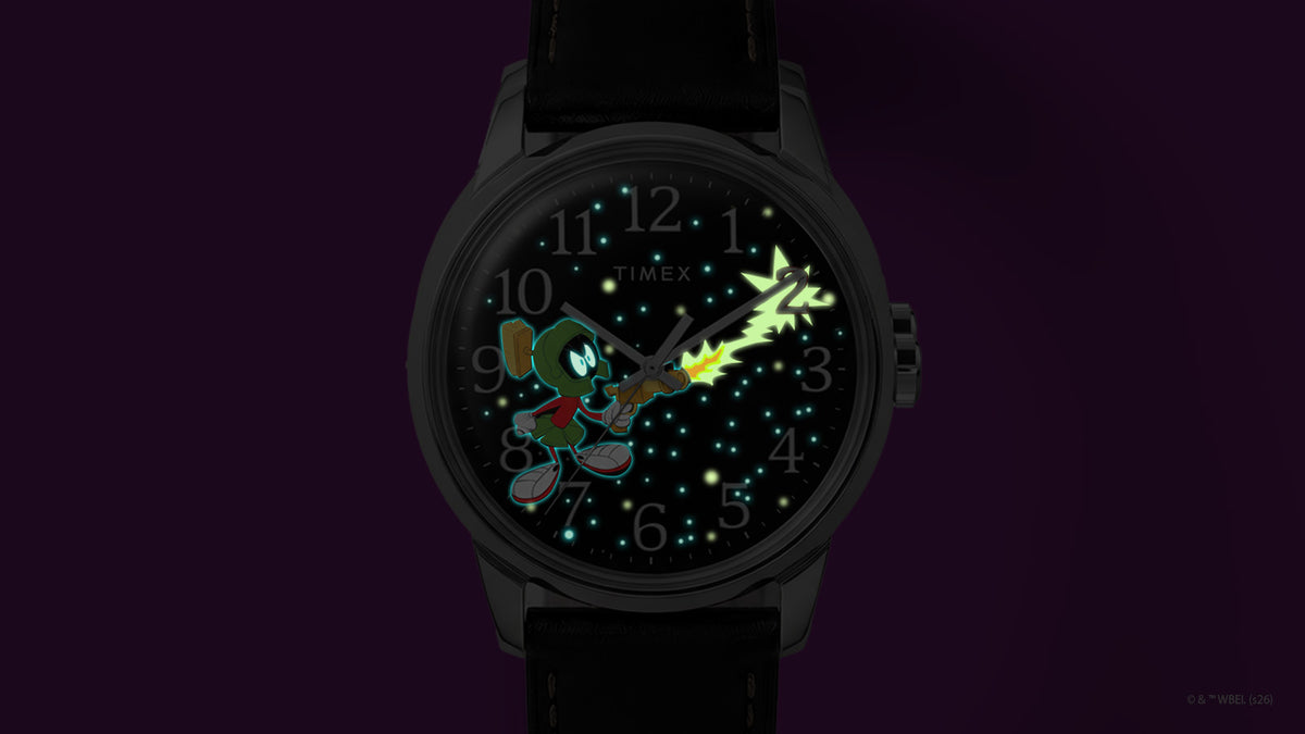 TW2Y99300 Marvin the Martian x Timex Easy Reader® watch showing stars and character details glowing blue-green, with a bright green ray-gun blast.