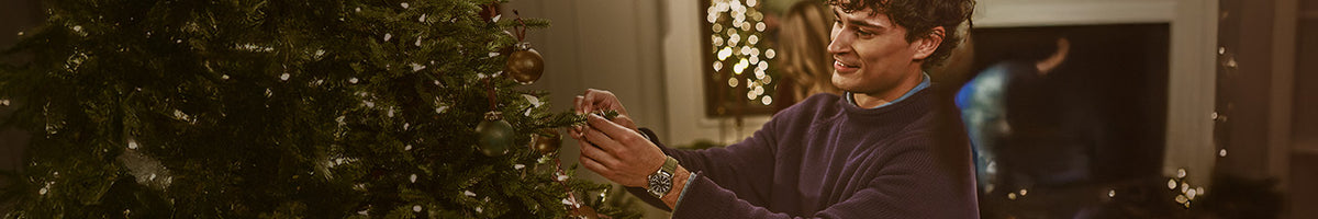 Gifts for Him - Man wearing a Timex watch with a green strap while decorating a Christmas tree.