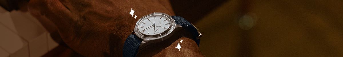 Luxe Gifts - Close-up of a Timex watch with a white dial, silver-tone case and navy strap worn on a wrist.