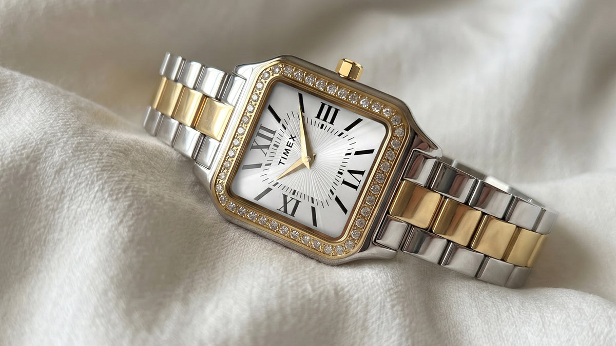TW2Y90400 Close-up of the Timex Addison watch on ivory fabric, showing its crystal-lined bezel and polished silver-and-gold-tone link bracelet.