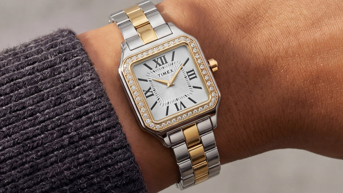 TW2Y90400 Close-up of the two-tone Timex Addison watch on a wrist, featuring gold-tone hands and a crystal-lined bezel beside a charcoal knit sleeve.