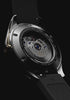 Timex Atelier GMT Première M1a watch rotating against a black background, highlighting its black and green GMT dial, gold-tone crown, rubber strap, and exhibition caseback.