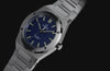 Close-up video of the stainless-steel Q Timex Marbella watch, highlighting its deep blue textured dial, luminous markers, polished bezel, and integrated bracelet against a dark background.