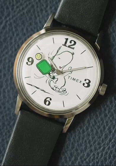 Product video of Peanuts® x Timex Marlin® Pickleball watch showcasing Snoopy pickleball dial animation, polished case details, INDIGLO® night-light feature, and engraved Peanuts caseback.