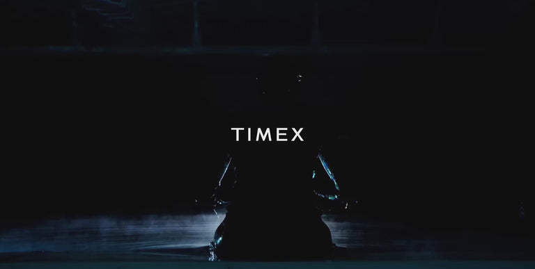 Underwater video of a free diver in a sleek wetsuit descending and floating calmly in a deep, tiled pool. The diver wears a wristwatch prominently visible throughout the movement. Gentle bubbles rise as the diver exhales and looks upward, capturing the serene and focused atmosphere of deepwater diving.