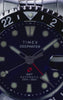 Timex Deepwater Meridian GMT Automatic watch with a blue dial and two-tone 24-hour bezel rotates against a blue background, highlighting its stainless-steel case, red GMT hand, and crown.